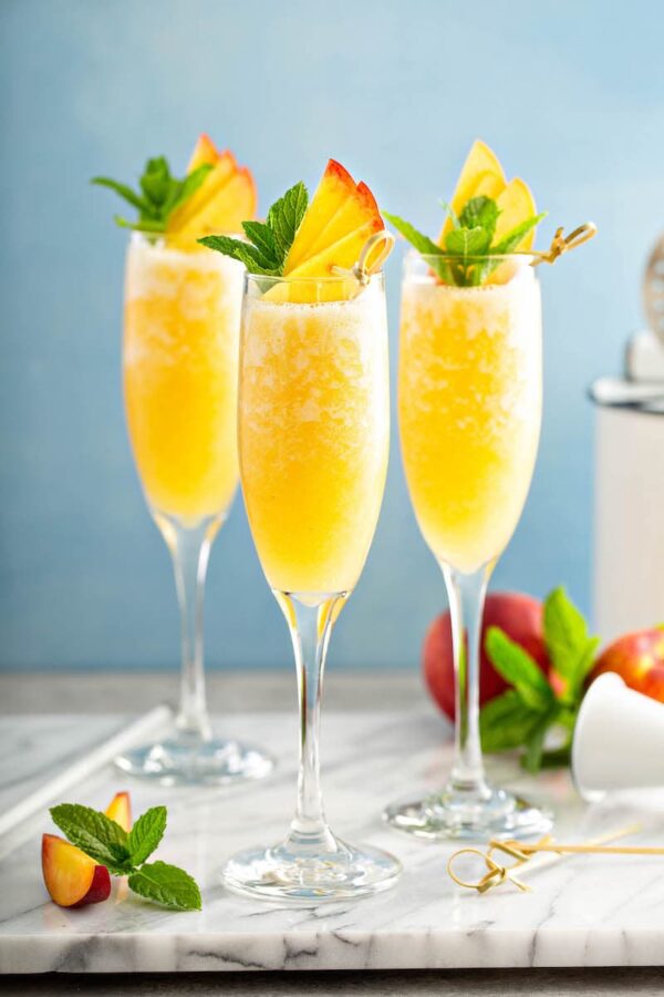 Three Peach Bellinis with fresh peaches on top. 