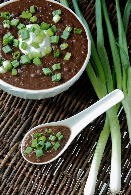 Black bean soup with green onions on top in a bowl with a spoon.