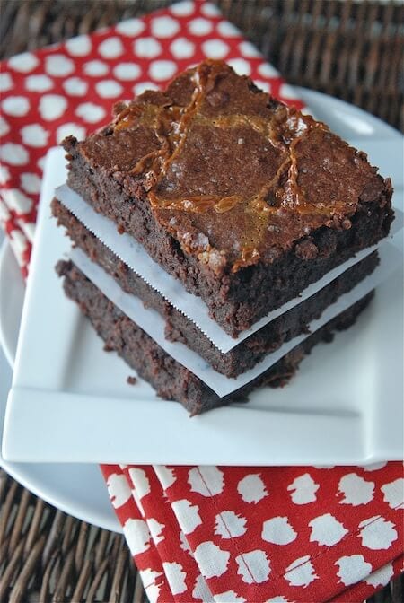 Three brownies stacked on top of each other on a white plate with a red napkin.