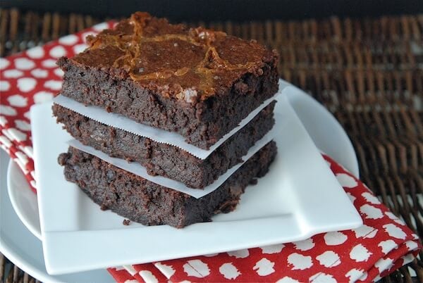Three brownies stacked on top of each other on a white plate with a red napkin.