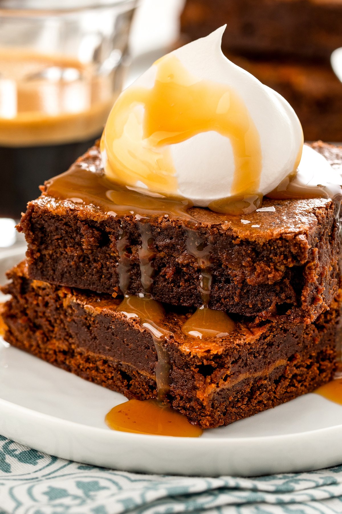 A stack of two salted caramel brownies with a caramel drizzle and whipped cream on top. 