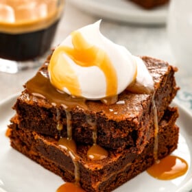 A stack of two salted caramel brownies with a caramel drizzle and whipped cream on top.