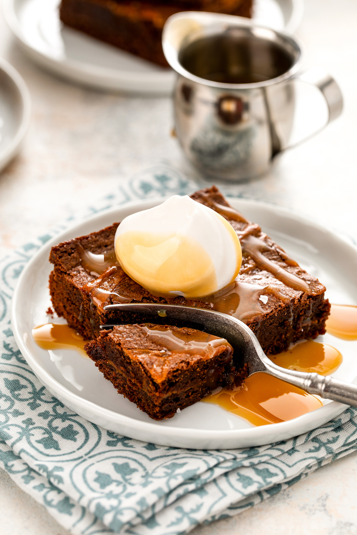 A sliced caramel brownie on a plate with fork cutting a bite.