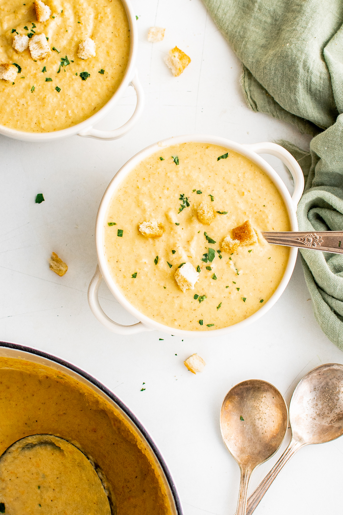 Two servings of soup in double-handled bowls, with soup spoons on the table nearby.