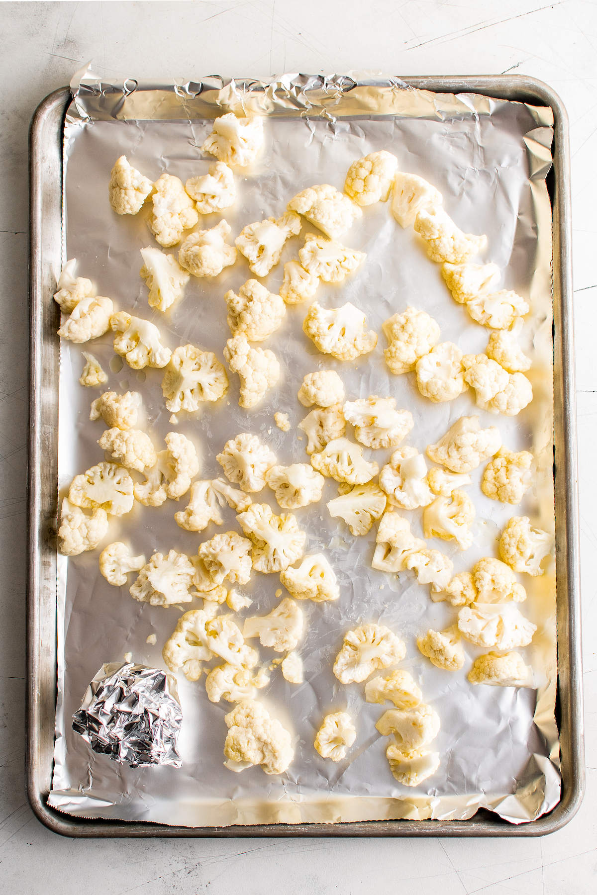 Cauliflower florets and a foil-covered head of garlic on a sheet pan.