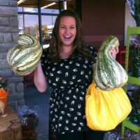 Girl holding two stripe cushaw squash out side of a grocery store.