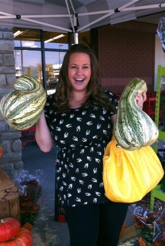 Girl holding two stripe cushaw squash out side of a grocery store.