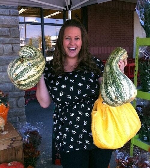 Girl holding two stripe cushaw squash out side of a grocery store.