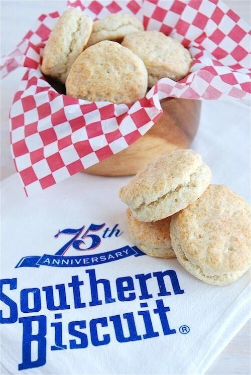 Three buttermilk biscuits stacked on top of each other with a bowl of biscuits behind it.