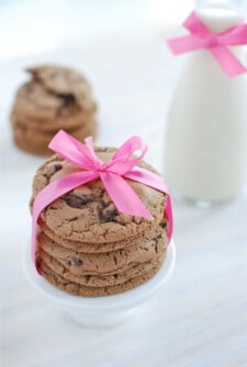 Triple Chocolate Malt Cookies stacked and tied with a pink bow and a jar of milk in the background