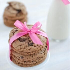 Triple Chocolate Malt Cookies stacked and tied with a pink bow and a jar of milk in the background