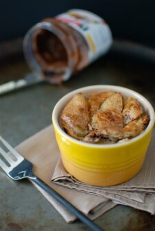 individual serving of nutella croissant bread pudding in a yellow dish with a fork and a jar of nutella in the background