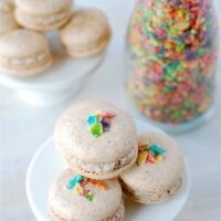 A Stack of Fruity Pebble Macarons on a White Stand with Another Stand and a Jar of Cereal in the Background