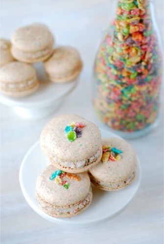 A Stack of Fruity Pebble Macarons on a White Stand with Another Stand and a Jar of Cereal in the Background