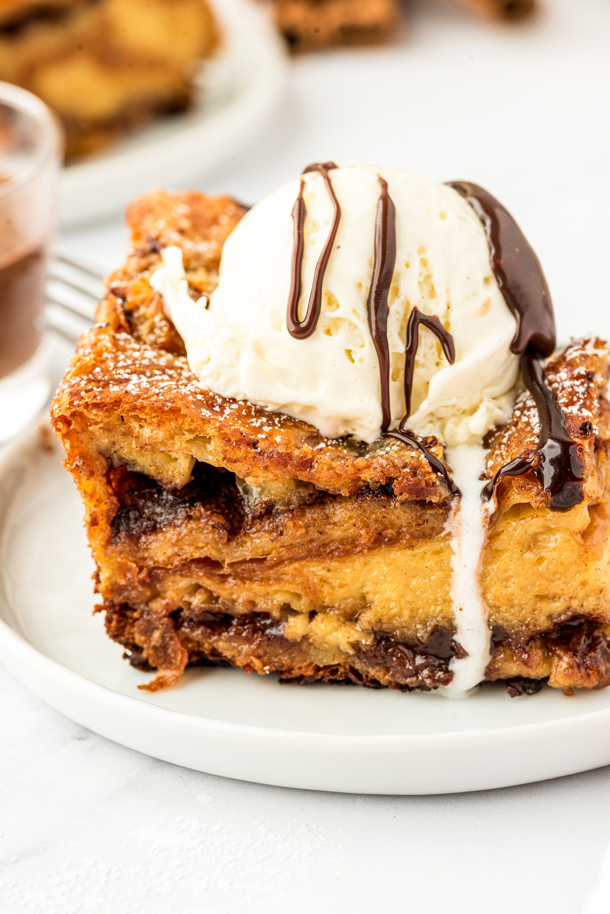 An edge piece of bread pudding with crispy sides, topped with ice cream and chocolate drizzle.