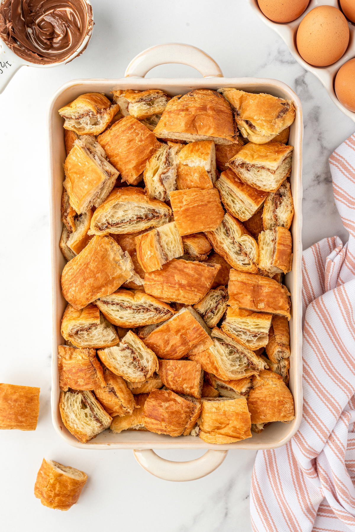 Small pieces of croissant sandwiched with Nutella, lining the bottom of a baking dish.