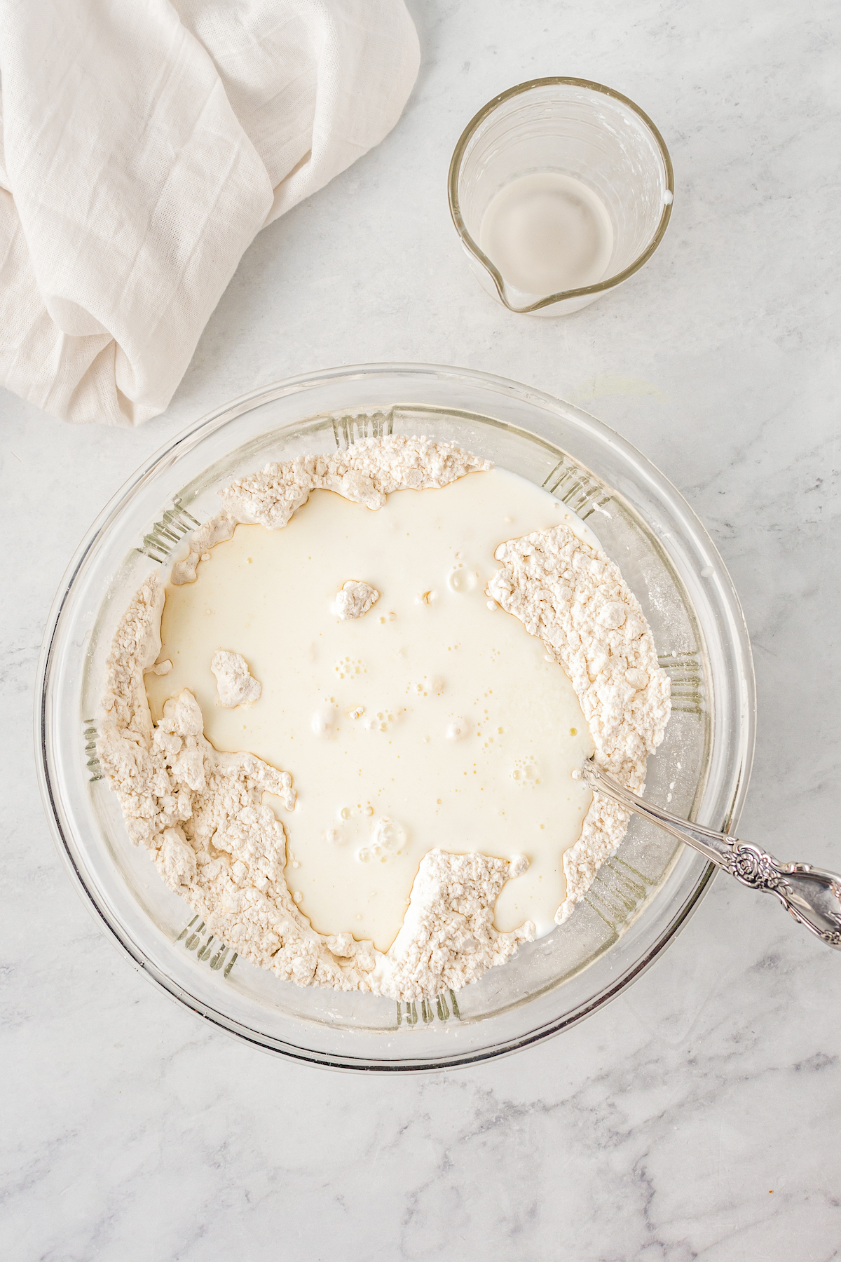 Buttermilk poured over dry baking ingredients in a glass bowl.