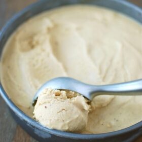 Brown butter ice cream in a pan with a ice cream scooper getting a scoop of ice cream.