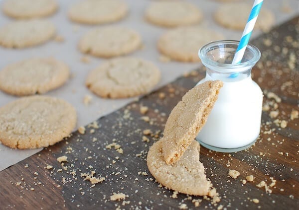 A sugar cookie split in half, set against a glass of milk.