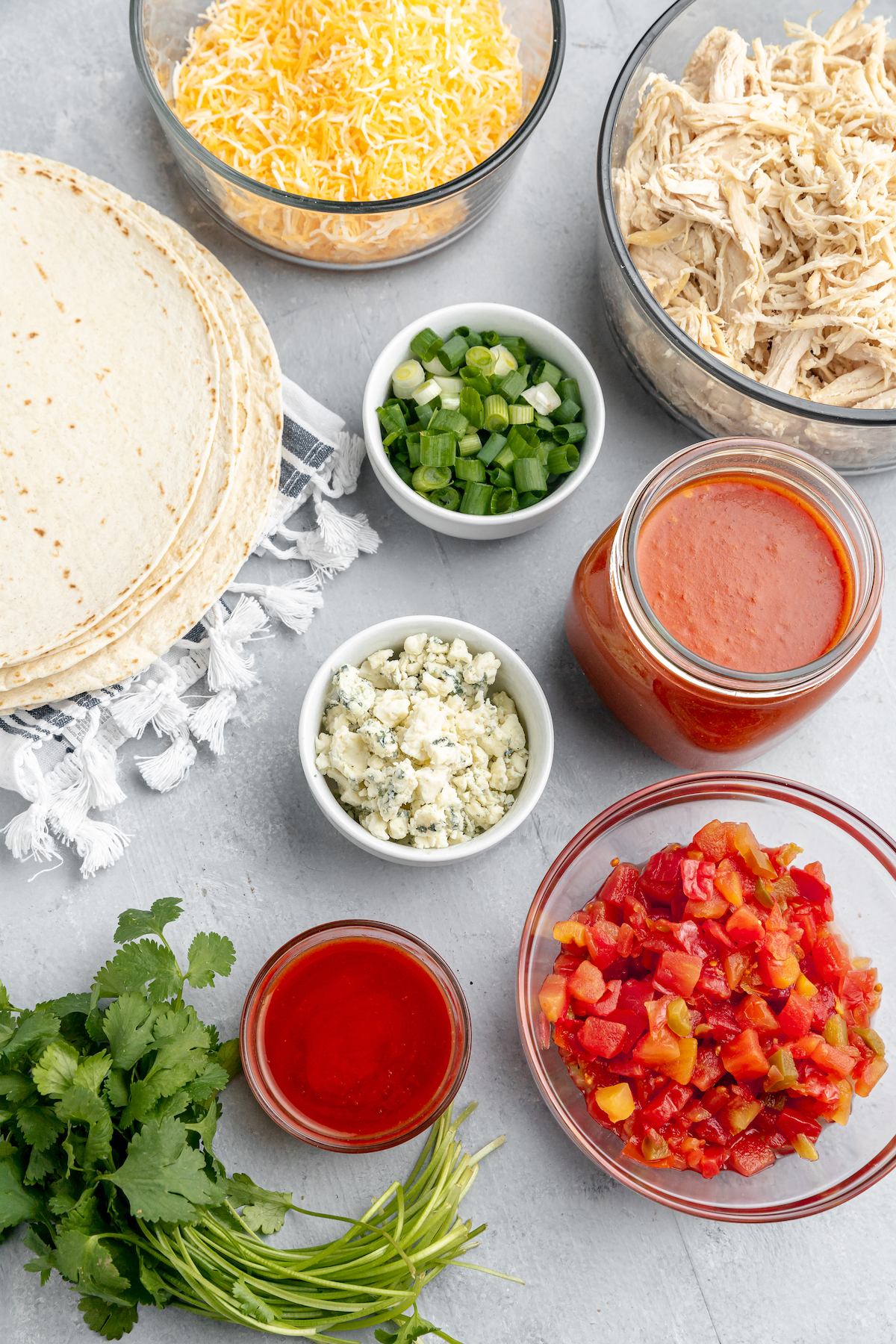 From top left: Flour tortillas, shredded cheese, shredded chicken, green onions, red enchilada sauce, bleu cheese, cilantro, buffalo wing sauce, diced tomatoes with green chilies.