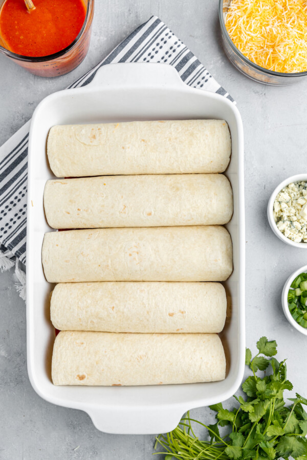 A row of rolled tortillas in rectangular baking dish.