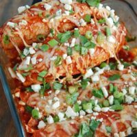 buffalo chicken enchiladas with green onions and blue cheese on top with a spatula pulling out enchiladas