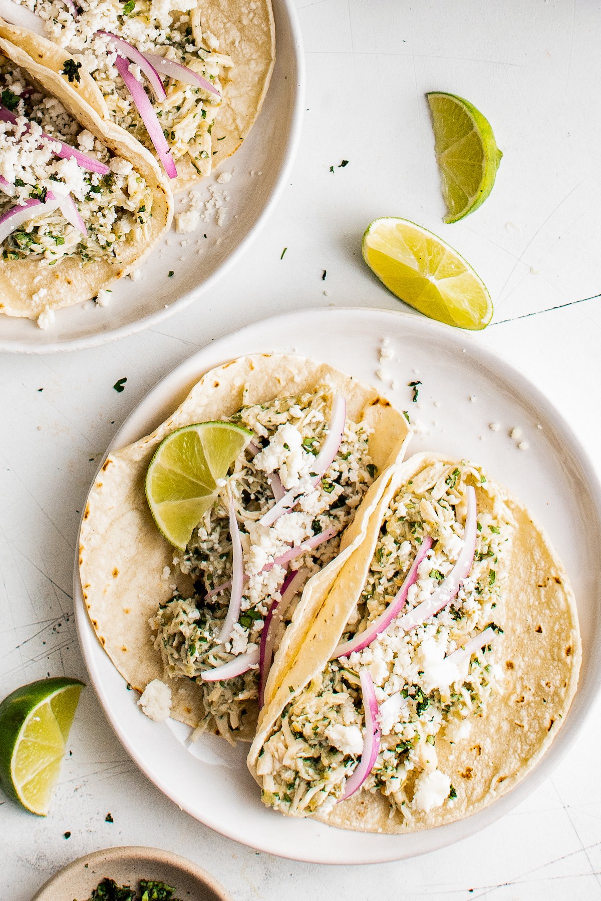 Chicken tacos on plates, garnished with lime and cotija cheese.