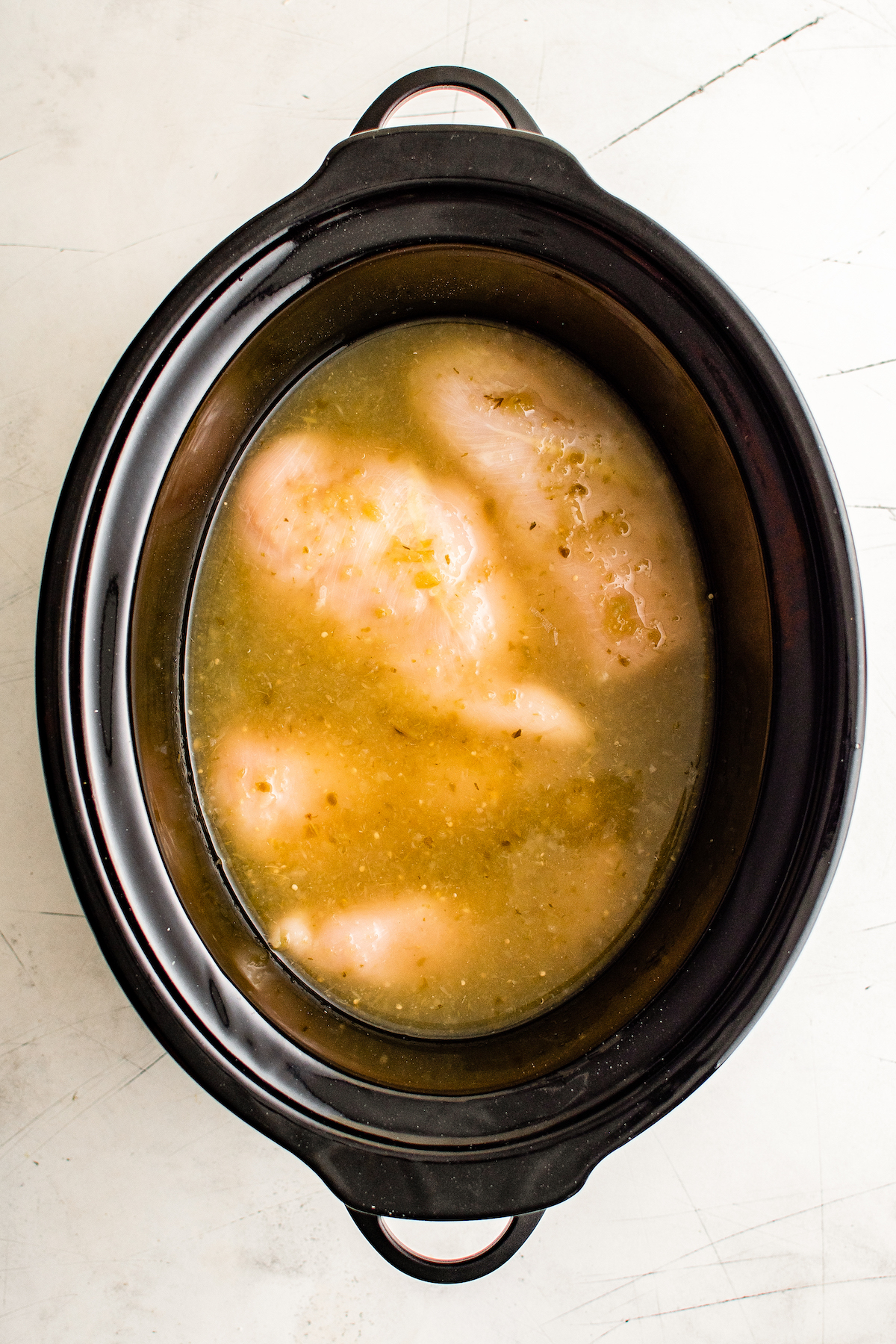 Chicken breasts in chicken broth and green salsa in a crockpot.