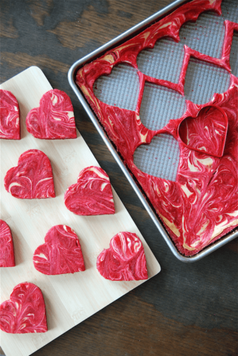 Red velvet brownies with cream cheese swirled through them in a baking pan being cut into hearts.
