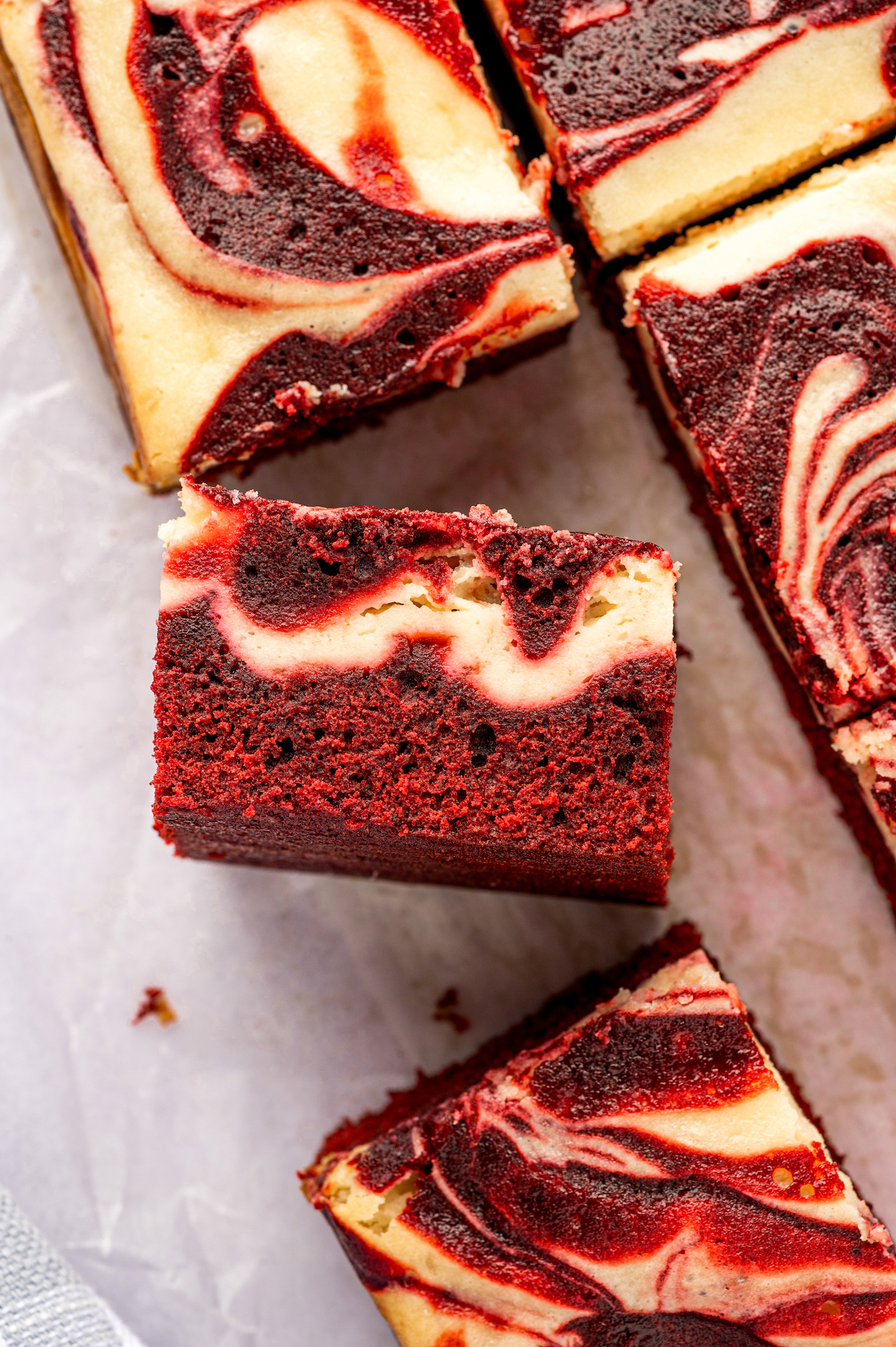 Red velvet cheesecake brownies turned on the side to show their visible red and white layers swirled together. 