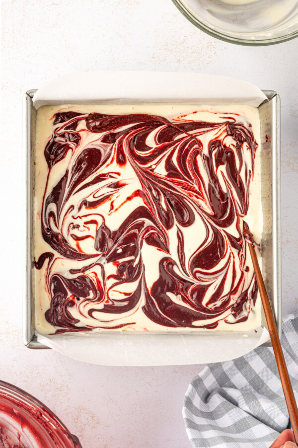 Cheesecake filing being swirled in red velvet brownie batter. 