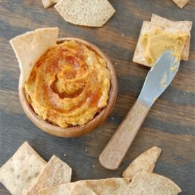 Overhead image of sweet potato hummus in a bowl with pita chips and a spreader knife.