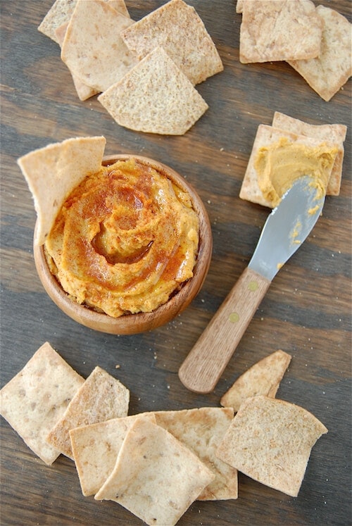 Overhead image of sweet potato hummus in a bowl with pita chips and a spreader knife.