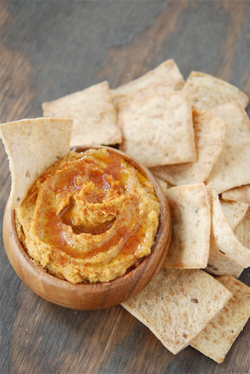 Sweet potato hummus with olive oil drizzled on top in a bowl with pita chips.