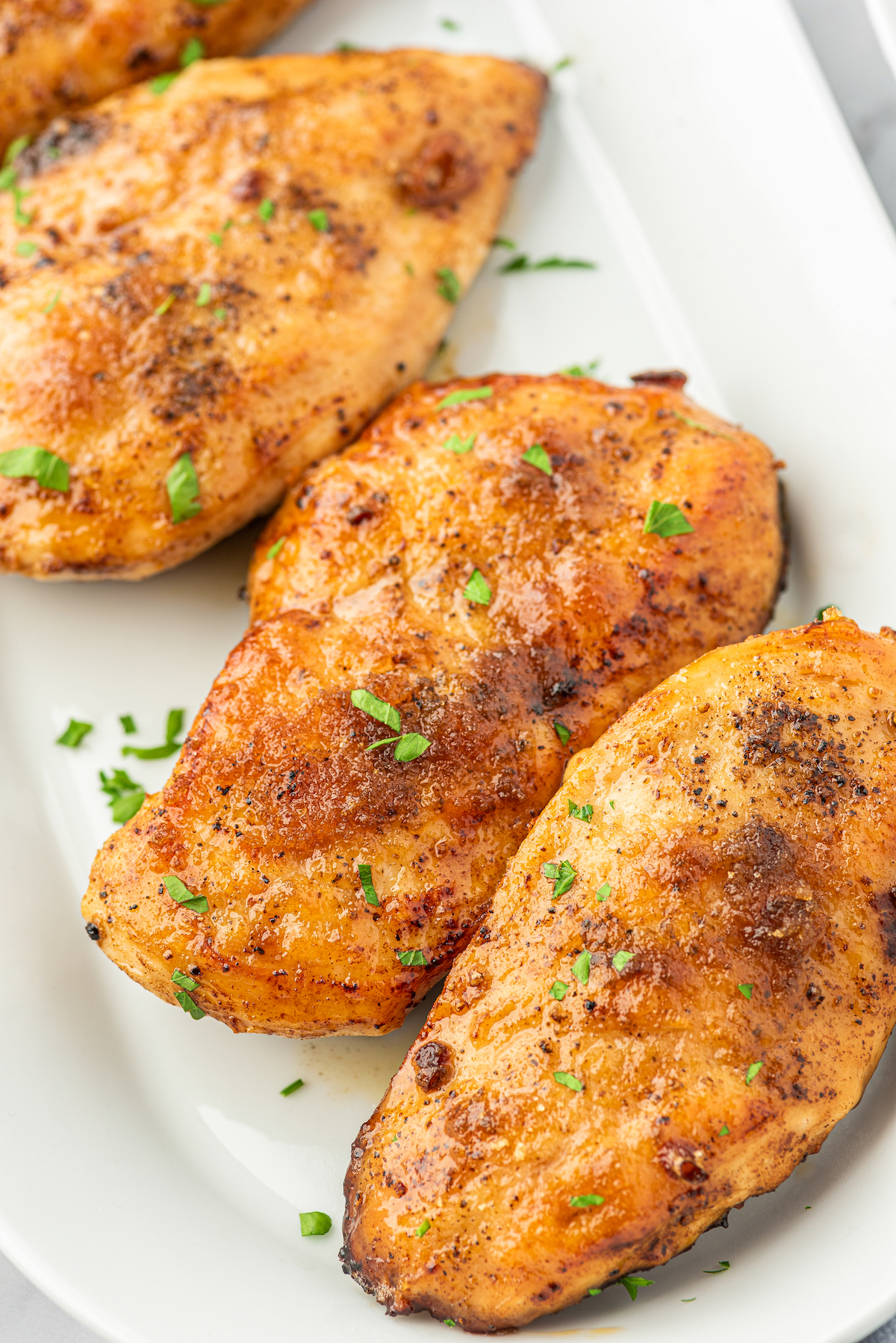 Tender and juicy garlic brown sugar chicken breasts on a serving plate topped with fresh herbs.