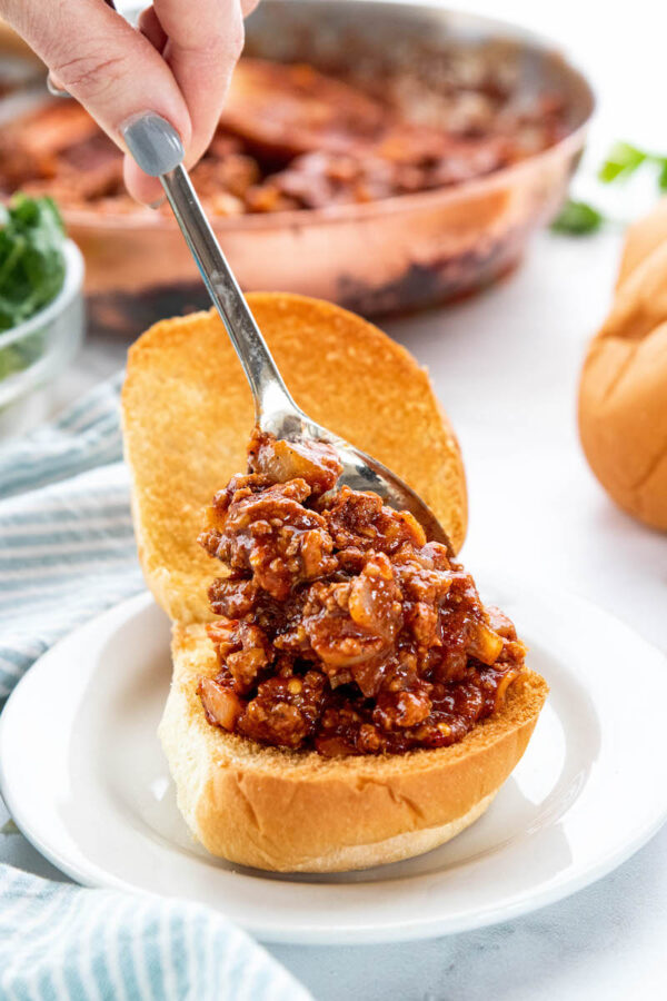Toasted buns with sloppy joe being put inside with a spoon.