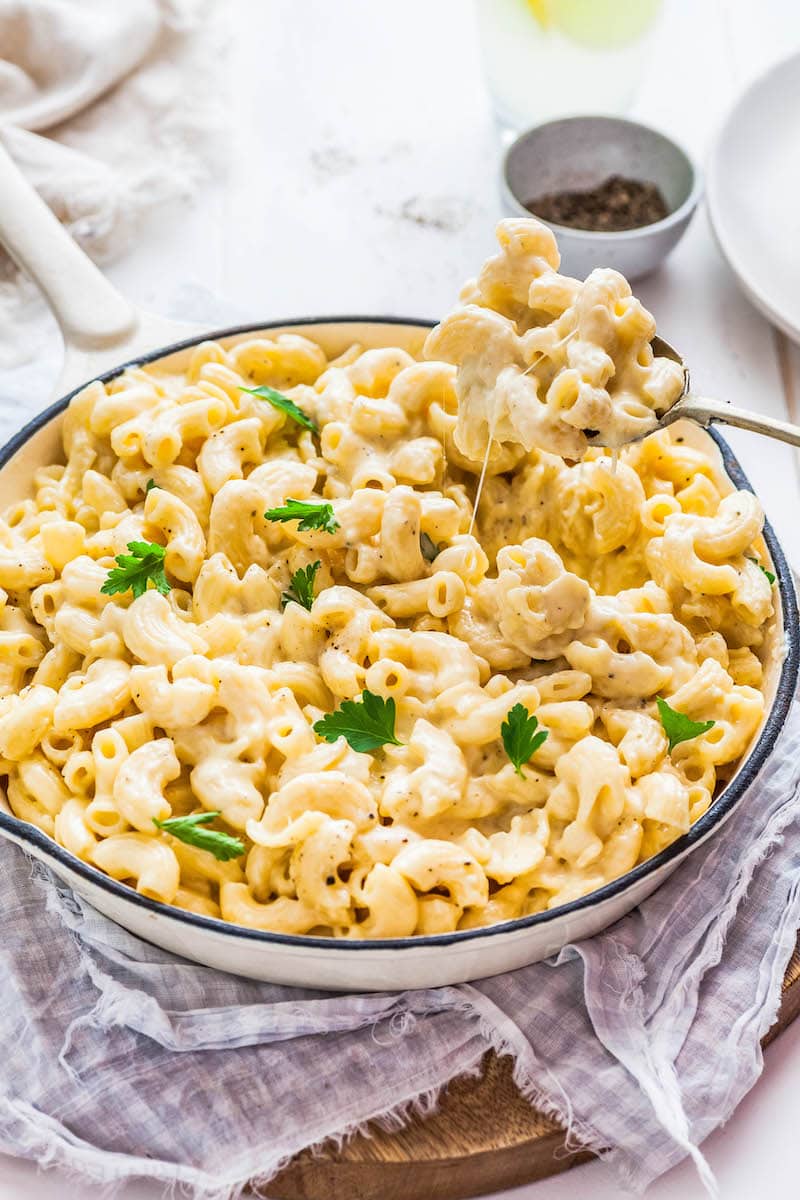 A serving spoon taking out a scoop of mac and cheese out of a skillet.