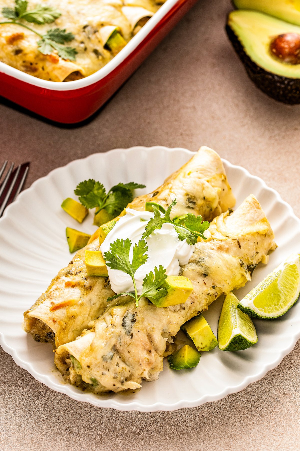 Two creamy white chicken enchiladas with lots of melted cheese topped with sour cream, avocado, and cilantro. 