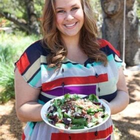 A woman in a colorful dress holding a white plate filled with salad