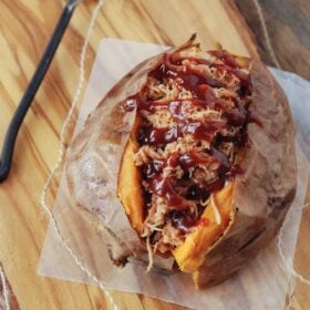 Pulled Pork Stuffed Sweet Potato topped with BBQ sauce on a wooden board