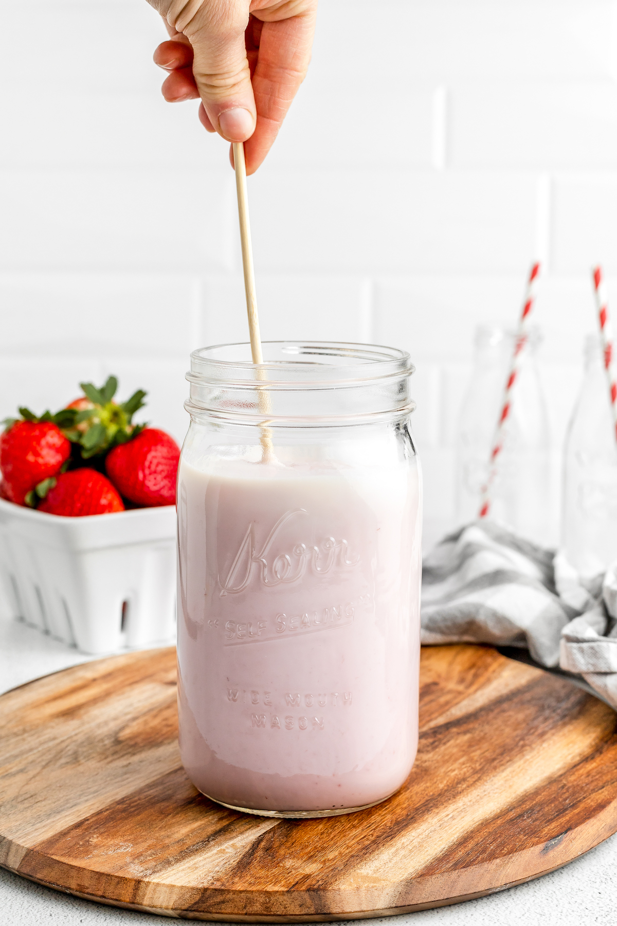 A woman's hand is stirring pink-tinted milk in a large mason jar.