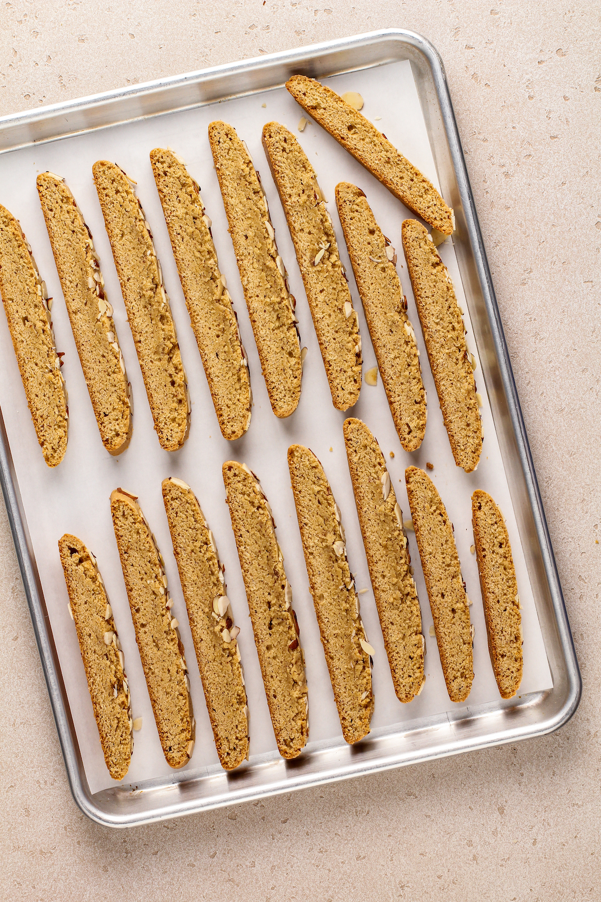 Slices of baked biscotti dough lined up on a baking sheet.
