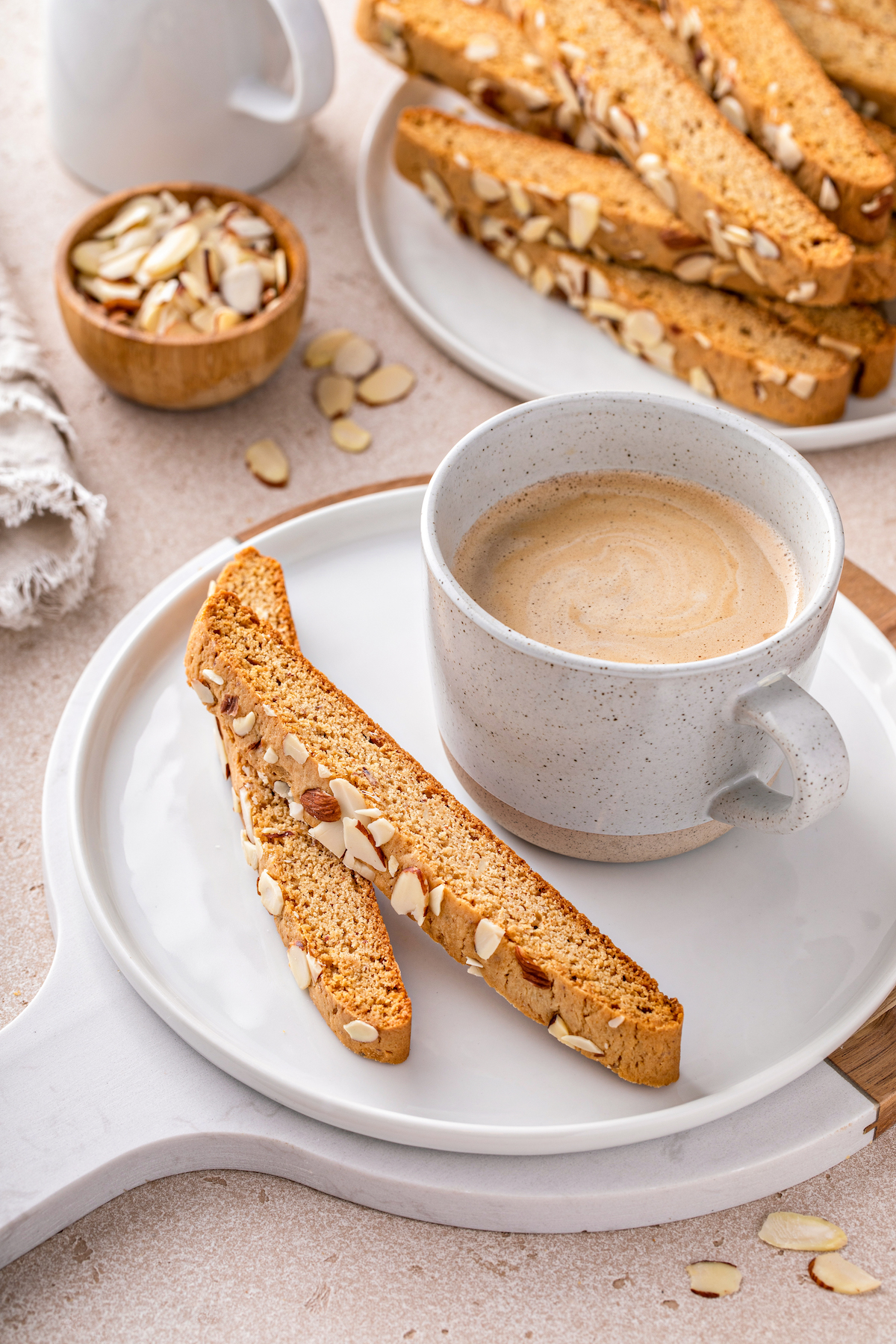 Two biscotti on a plate next to a small cup of coffee.