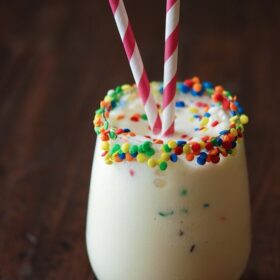 Close up photo of Cake Batter Milkshake with pink and white straws and colorful candy rimmed glass