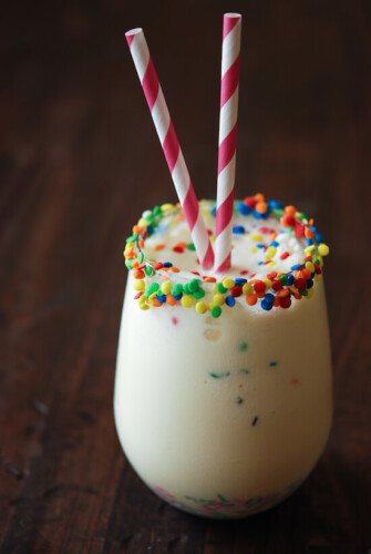 Close up photo of Cake Batter Milkshake with pink and white straws and colorful candy rimmed glass