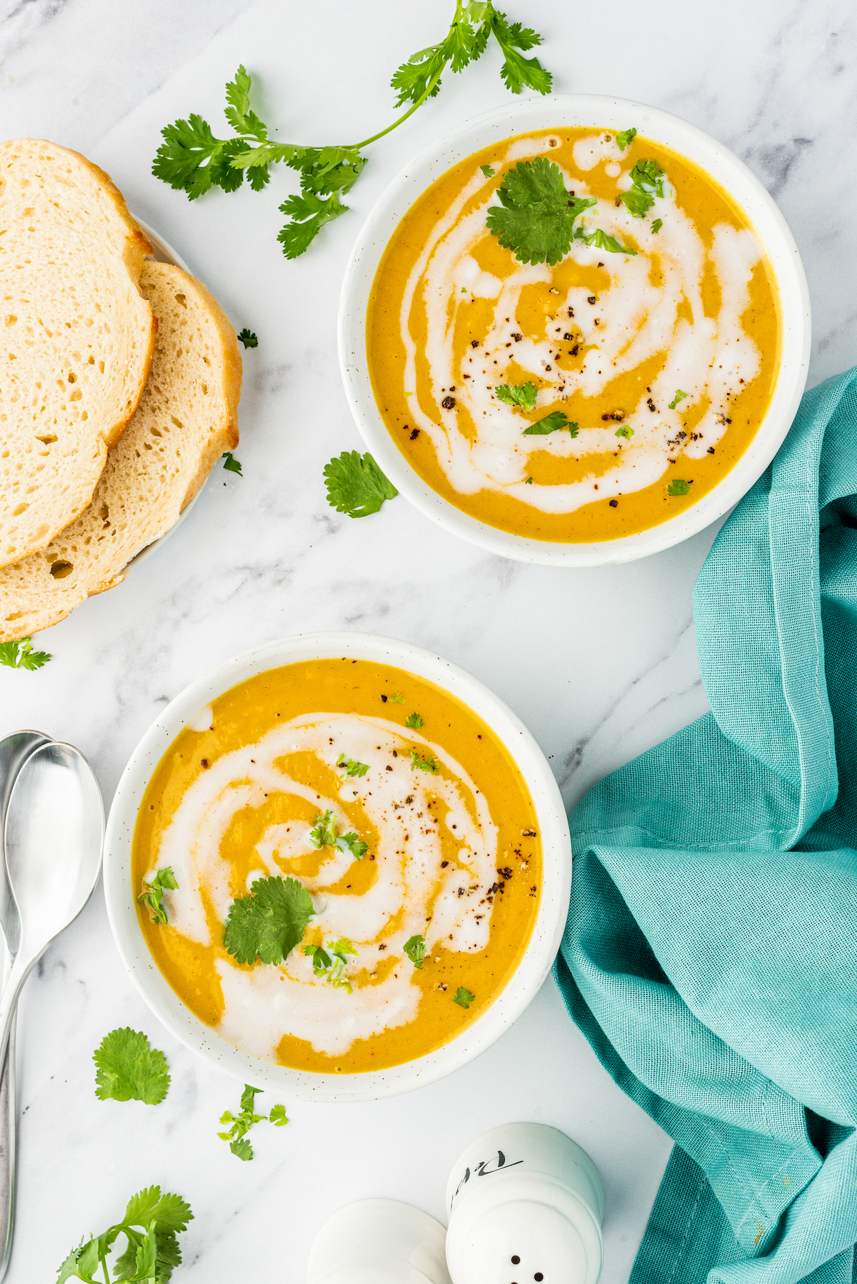 two bowls of butternut squash coconut curry soup with cream swirls and green herb garnish