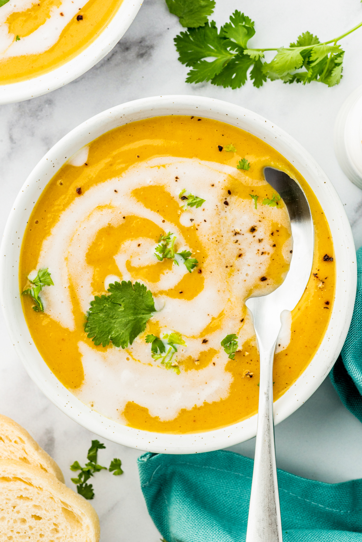 a bowl of butternut squash soup with a cream swirl and herb garnish with a spoon in it