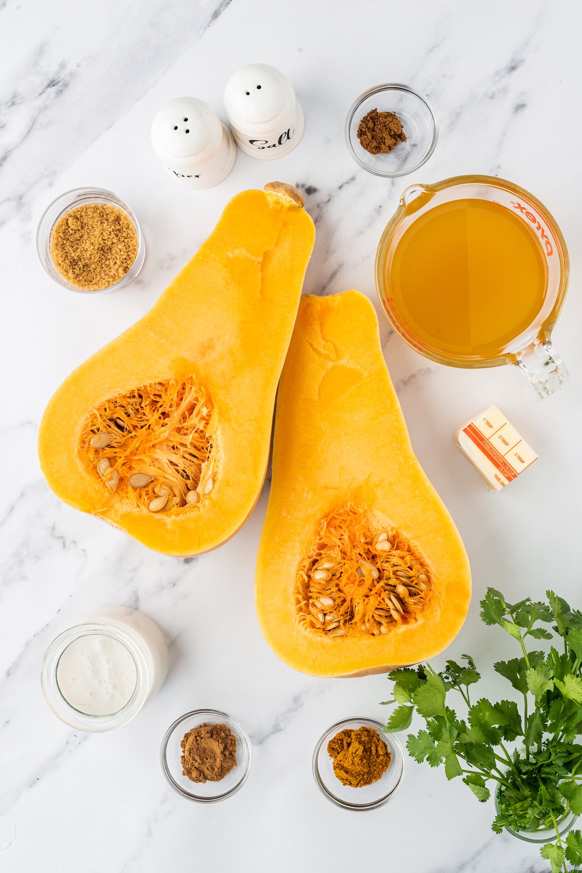 butternut squash cut in half lengthwise alongside spices, butter, and stock on a countertop