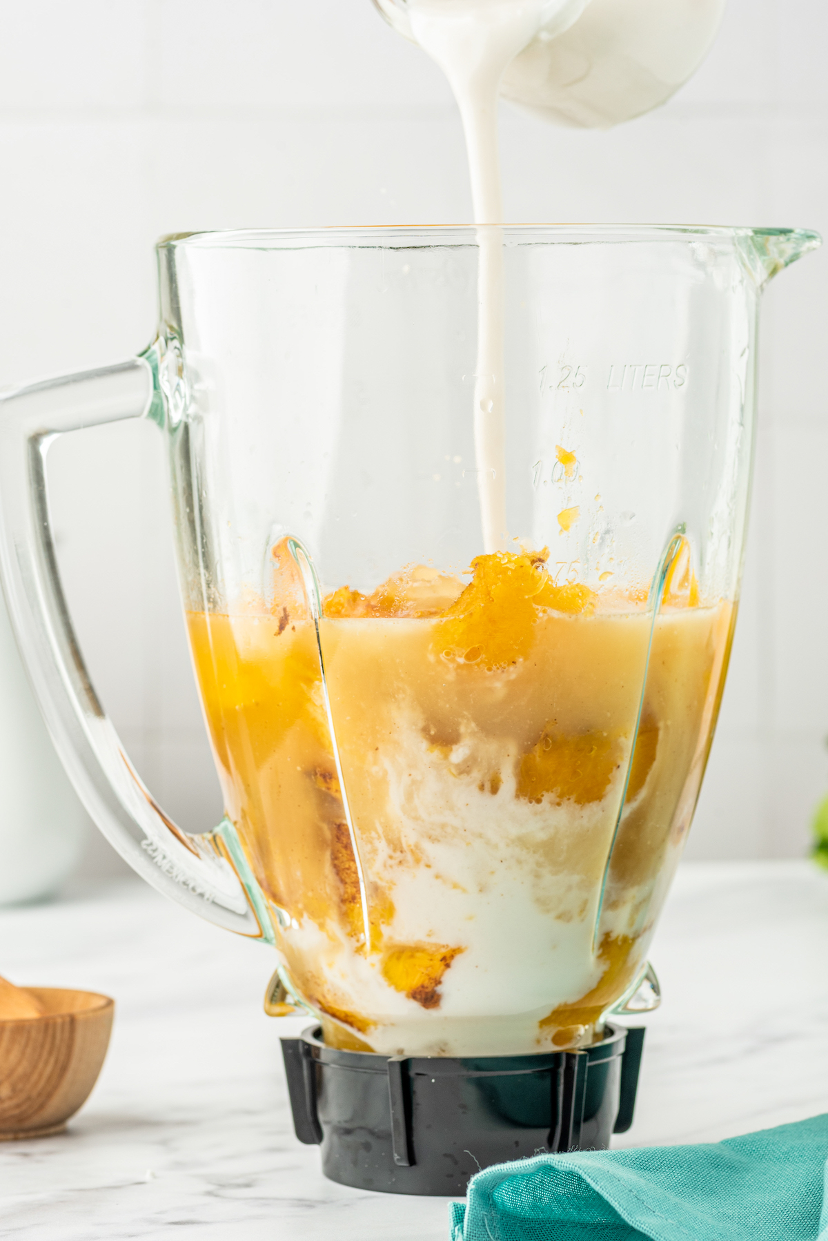 cooked chunks of butternut squash in a blender cup with stock and coconut milk being poured in
