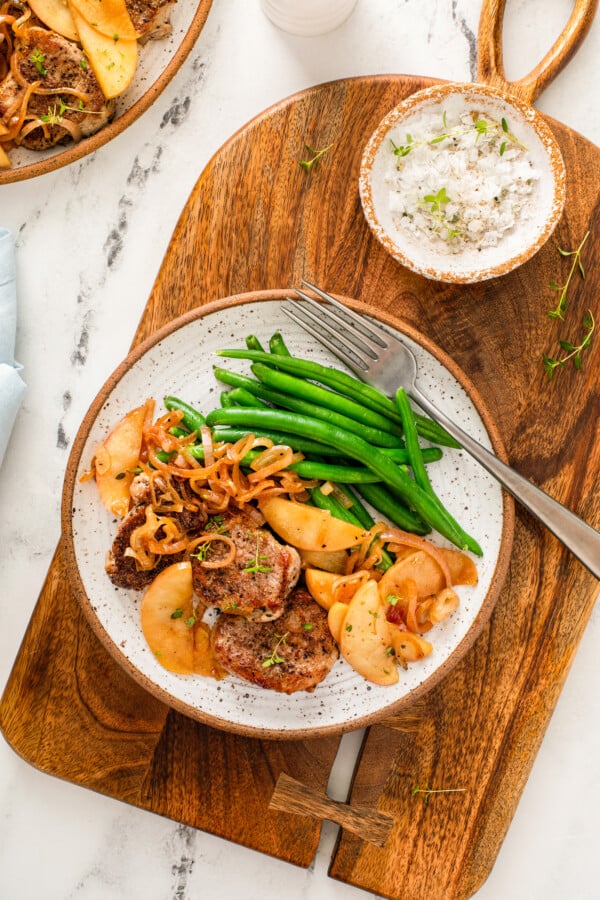 Pork with apples is plated with a fork and green beans. 